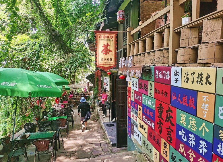 A narrow street with outdoor seating, a green umbrella, and colorful signs. 1
