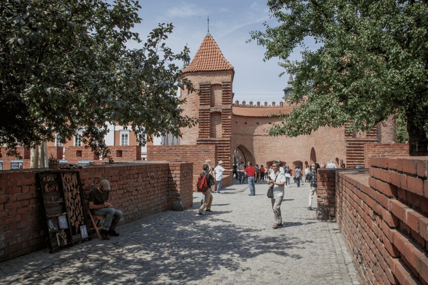 A historic brick wall with a tower, a cobblestone path, and people walking. 2