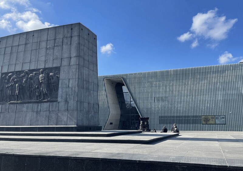 A modern building with a large relief sculpture on the left and a unique curved entrance. 4