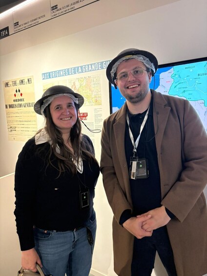 Two people standing in front of a wall with historical posters and a map. 3