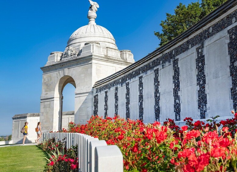 A monument with a dome and an archway, surrounded by red flowers. 1