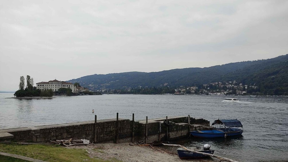 A calm lake with boats docked, a large white building, and a forested hill in the background. 3