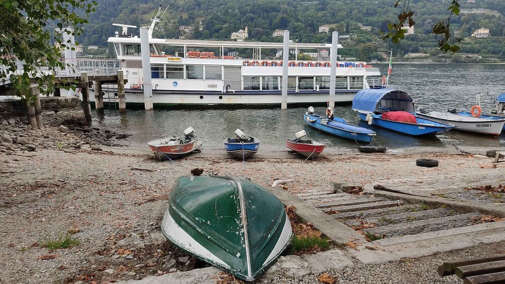 A ferry dock with several boats, a green boat on the shore, and a mountainous landscape in the background. 2