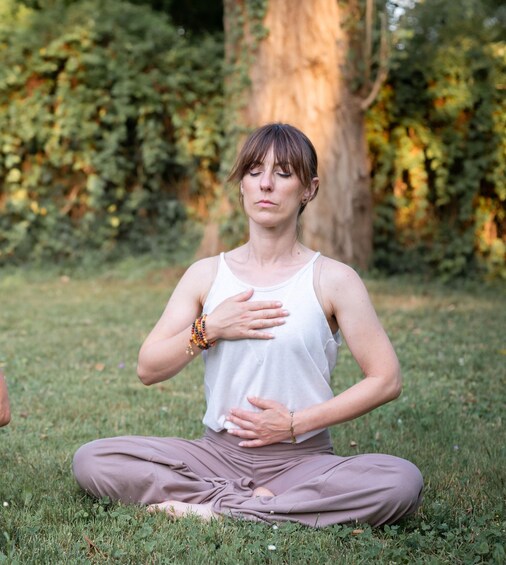 A person sitting cross-legged on grass in a park with trees and foliage in the background. 1