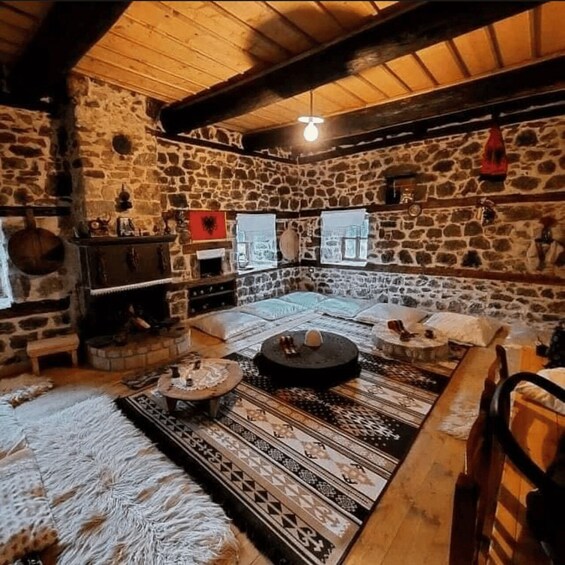 A rustic stone-walled room with a wooden ceiling, a patterned rug, and a traditional fireplace. 1