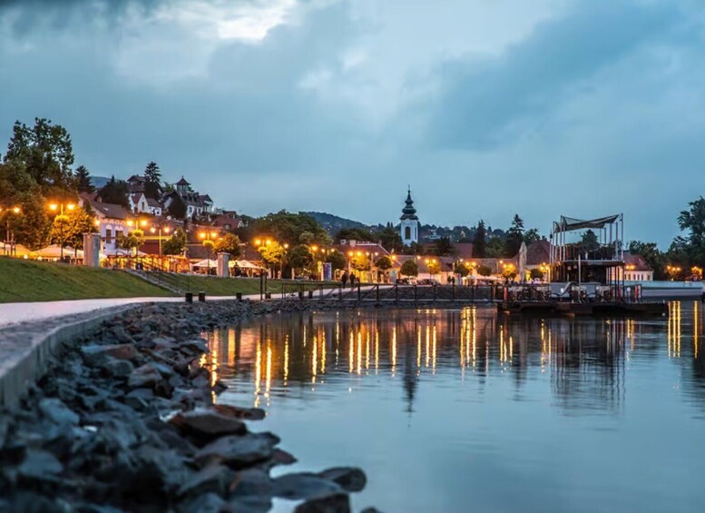 A riverside town at dusk with illuminated buildings and a calm water reflecting the lights. 4