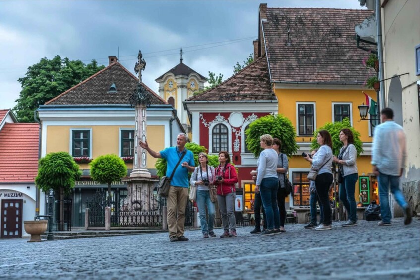 A cobblestone street with tourists, colorful buildings, and a church tower. 5