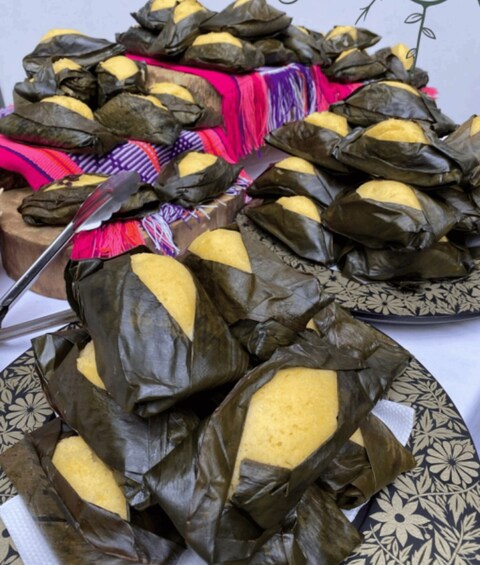 A variety of traditional foods wrapped in leaves, displayed on a table with patterned tablecloths. 2