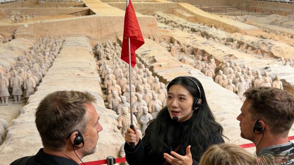 A person holding a red flag in front of a large number of terracotta soldiers. 1