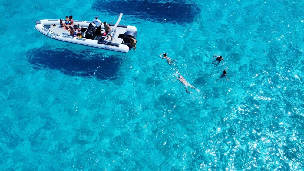 A group of people swimming and a boat in clear blue water. 4