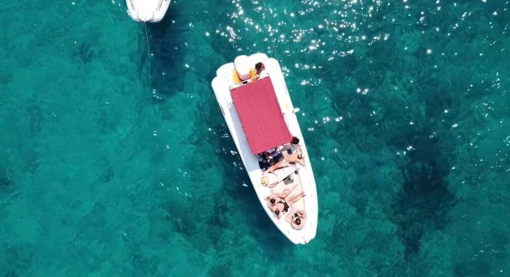 A white boat with a red cover and two people on it, floating on clear turquoise water. 1
