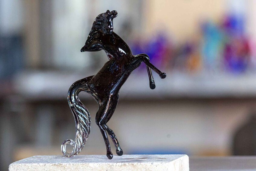 A black glass sculpture of a rearing horse on a white pedestal. 3