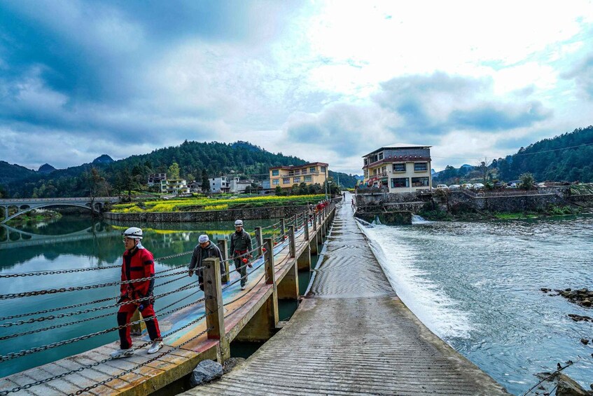 A wooden bridge over a river with people walking, surrounded by hills and buildings. 5