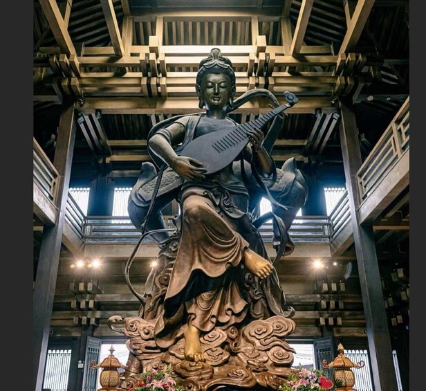 A large statue of a seated figure with a musical instrument, surrounded by ornate carvings and traditional lamps. 3