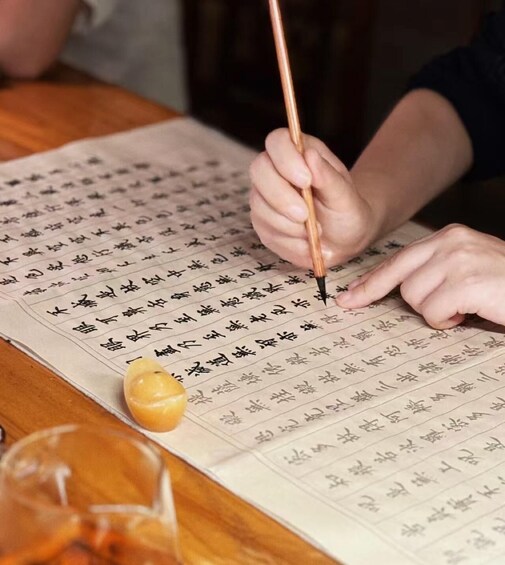 A person writing Chinese characters on a large sheet of paper with a traditional brush pen. 1