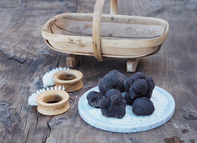 A rustic wooden basket, a plate with black truffles, and two wooden scoops on a wooden surface. 3