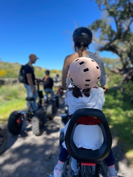A child on a tricycle with a helmet, an adult on a motorcycle, and another adult on a bicycle. 4