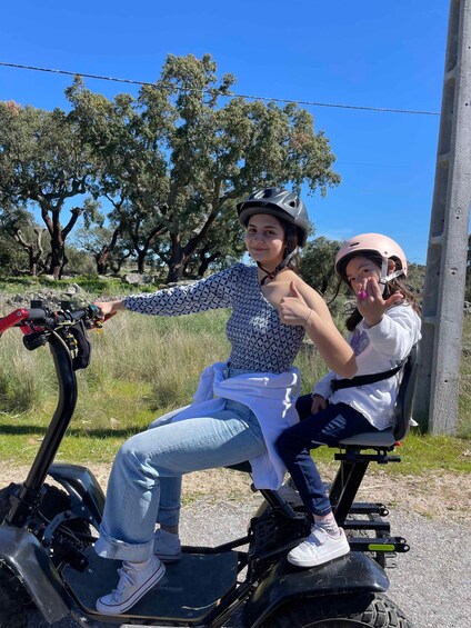 Two people on an electric scooter in a natural setting with trees and a clear sky. 5