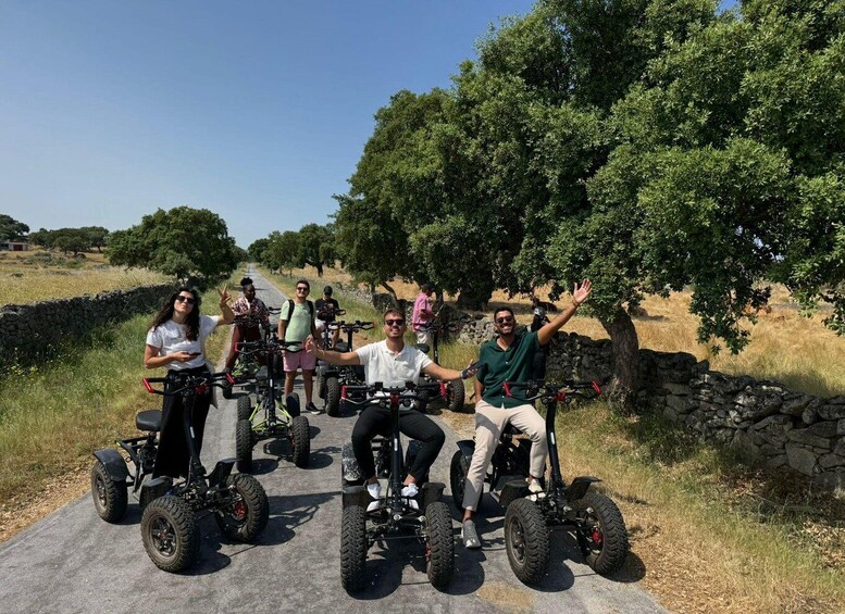 A group of people on electric all-terrain vehicles on a paved path in a rural setting with trees and stone walls. 2