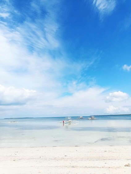 A beach with calm waters, a clear sky, and a few boats anchored in the distance. 1