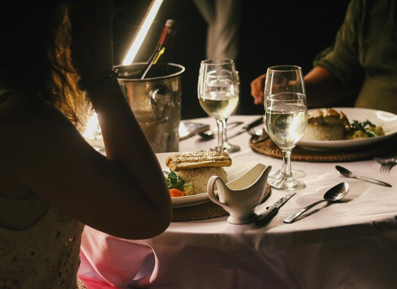 A dimly lit dining table with a candle, a glass of water, a glass of white wine, a plate with food, and a pitcher. 2