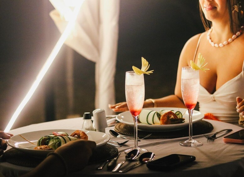 A dining table with two champagne flutes garnished with flowers, a plate of food, and a salt and pepper shaker. 1