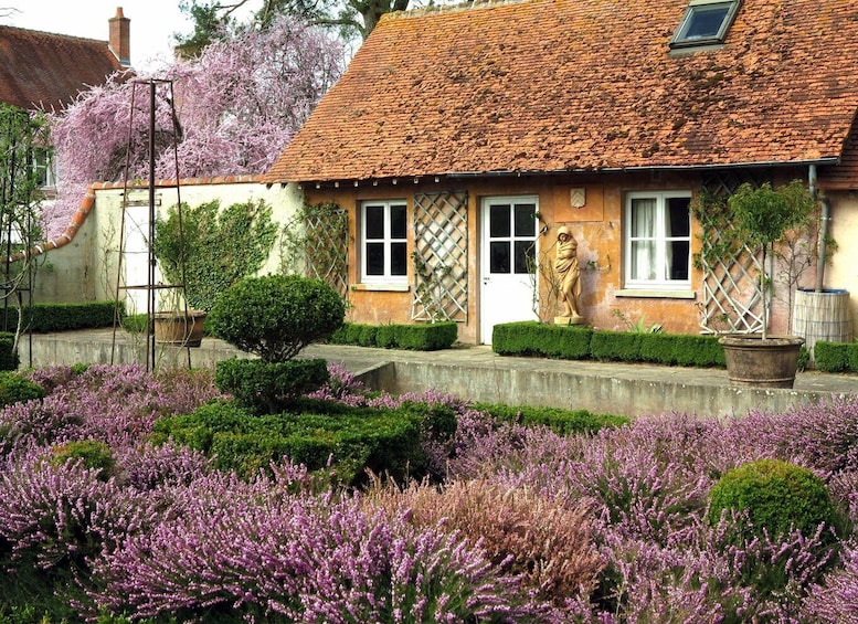 A house with a tiled roof, a statue, and purple heather in the garden. 4