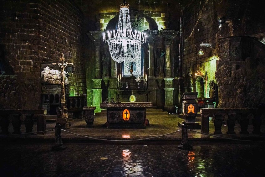 A dimly lit interior with a large chandelier, a central altar, and stone walls. 5