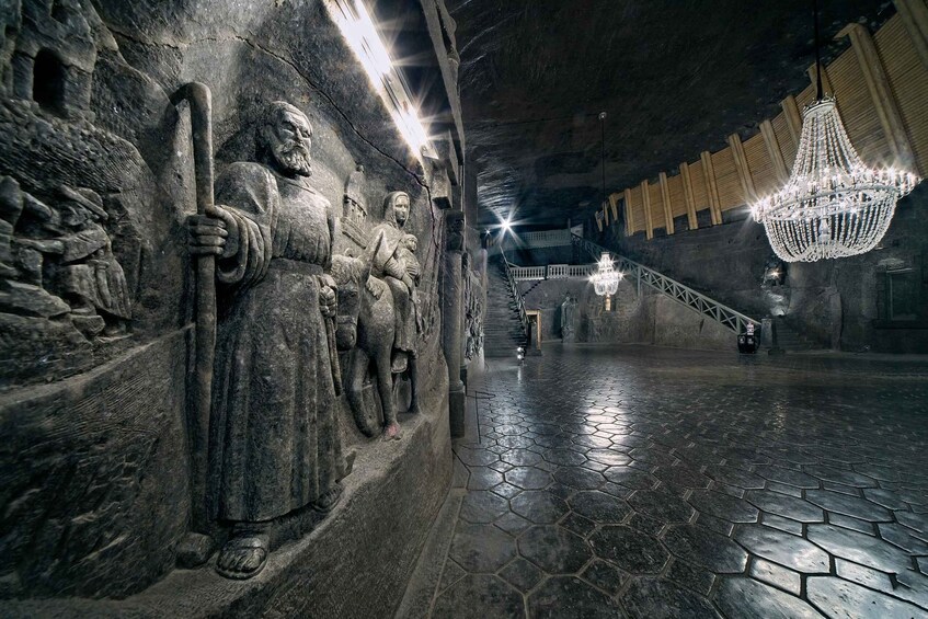 A stone-carved statue, a staircase, and a chandelier in a dimly lit underground passage. 1