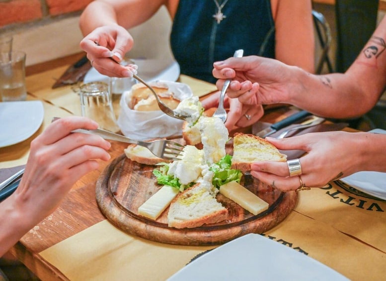 People at a table with a wooden board, cheese, and bread. 3