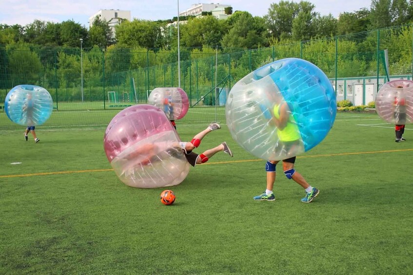 People playing soccer inside transparent balls on a field. 1