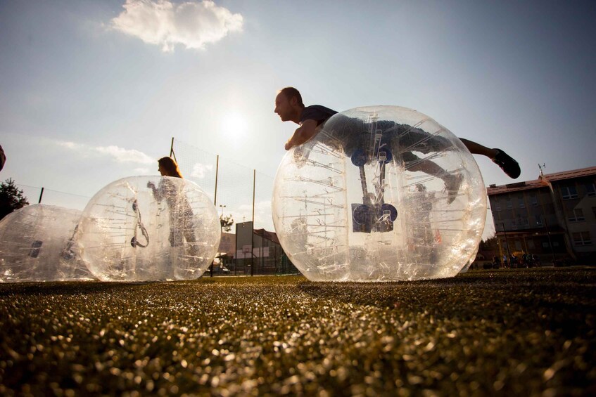People inside transparent spheres on a grassy field. 2