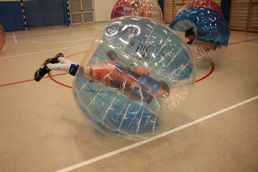 People inside transparent spheres on an indoor court. 3