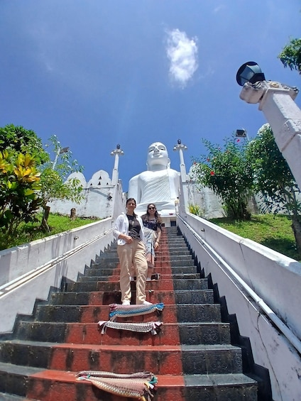 A large white statue at the top of a staircase with two people ascending. 1