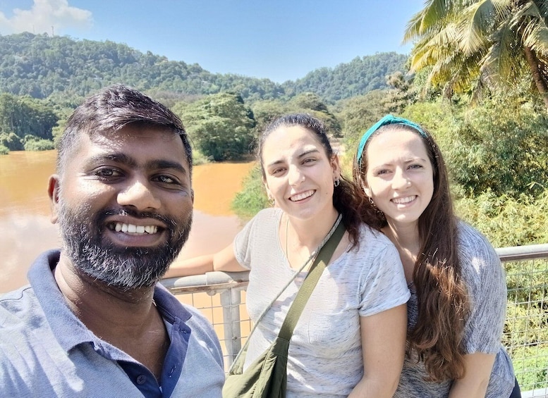 Three people near a river with a forested hill in the background. 1