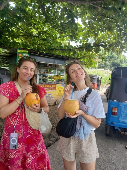 Two women holding coconuts, a street food stall, and an auto-rickshaw in the background. 5
