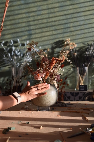 A hand holding a vase with dried flowers and greenery. 3