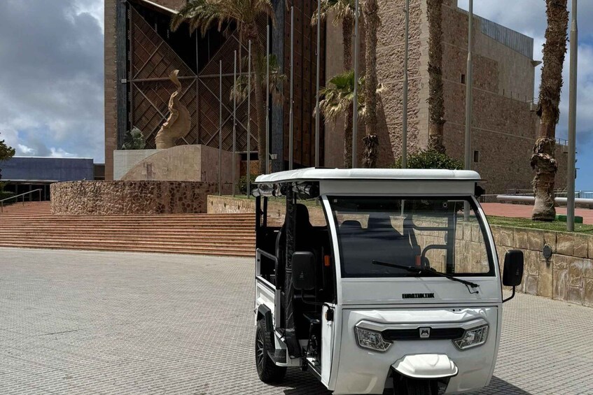 A white golf cart parked in front of a modern building with a stone facade and palm trees. 5