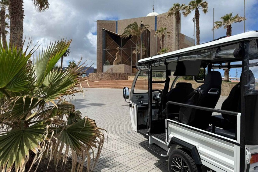 A white safari vehicle parked in front of a building with a modern design, palm trees, and a clear sky. 3