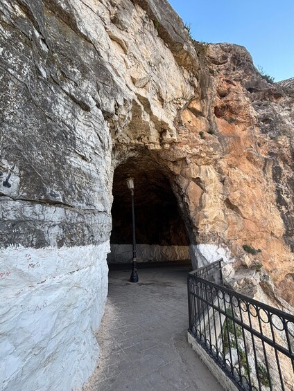 A cave entrance with a metal railing and a street lamp inside. 4