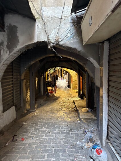 A narrow alley with brick pavement, closed shops, and overhead wires. 3