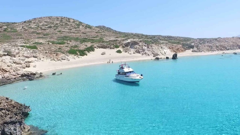 A boat on a clear turquoise sea with a rocky coastline and a sandy beach in the background. 2