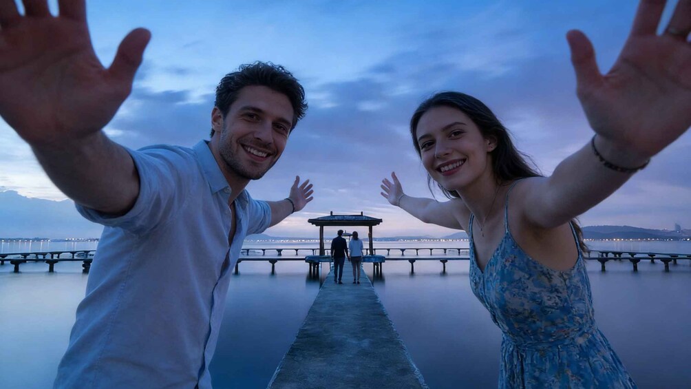 A couple with outstretched arms on a pier with a calm body of water and a distant cityscape. 1