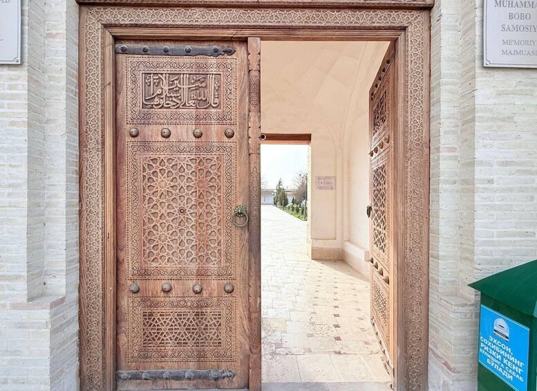 An intricately carved wooden door with Arabic calligraphy, leading to a courtyard with a tiled pathway. 2