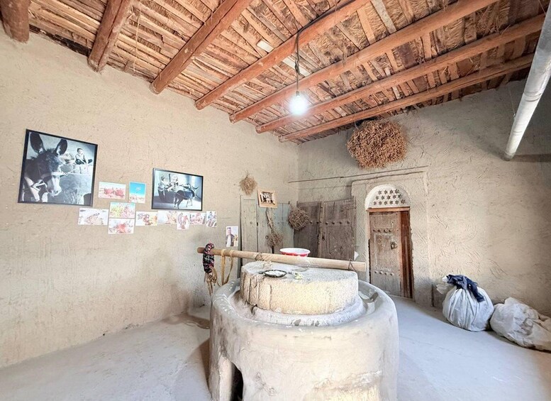 A rustic interior with a wooden ceiling, a stone mill, and various photographs on the wall. 5