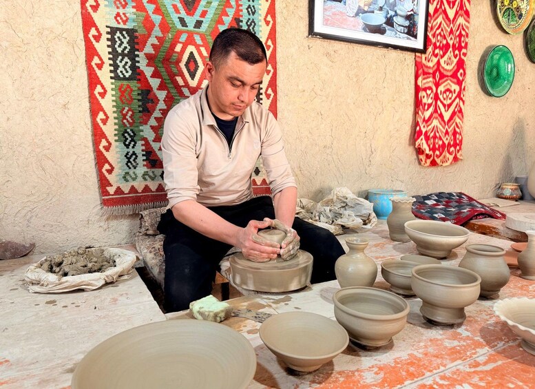 A person shaping a clay pot on a pottery wheel in a workshop with various unfinished pots and pottery tools. 3