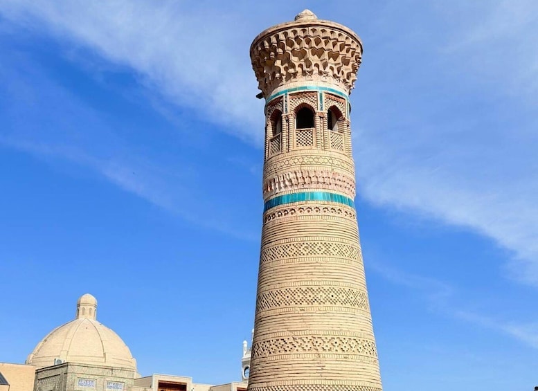 A tall, intricately patterned minaret with a dome structure in the background. 1