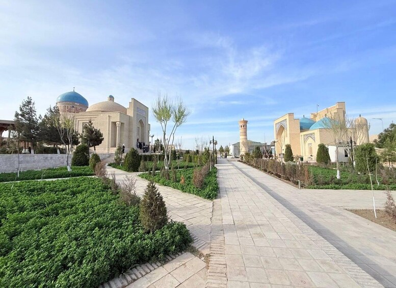 A pathway leading to a mosque with a minaret and dome, surrounded by greenery and other buildings. 3