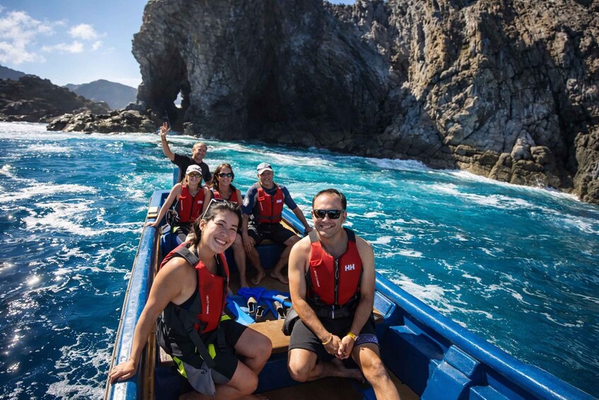 A group of people on a boat wearing life jackets, surrounded by clear blue water and rocky cliffs. 5