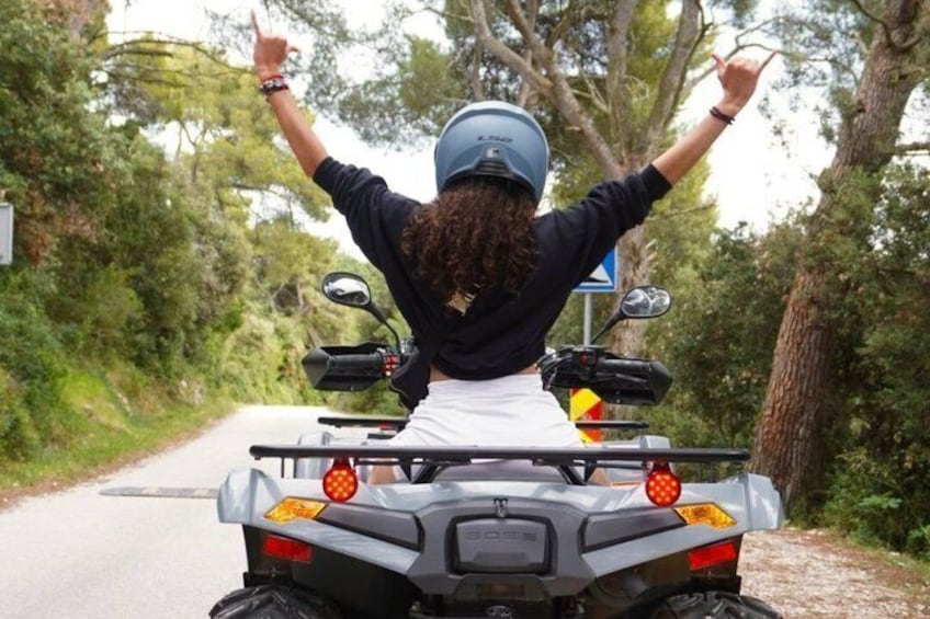 A person riding a quad bike on a narrow road surrounded by trees. 1